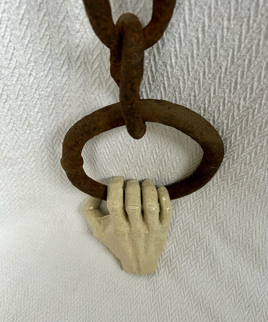 Stoneware sculpture depicting a hand losing grip on a metal ring held with a long chain.